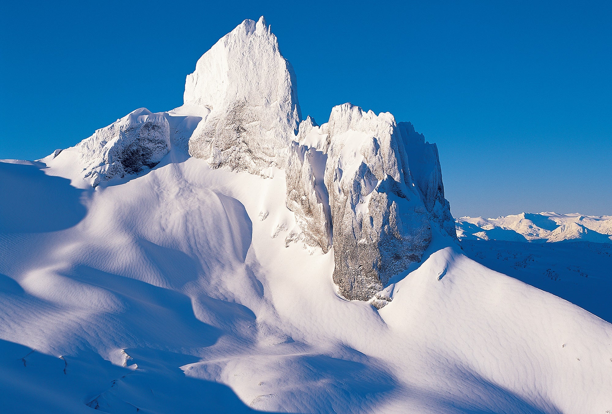 A jagged peak juts out from thick snowy slopes. End of image description.