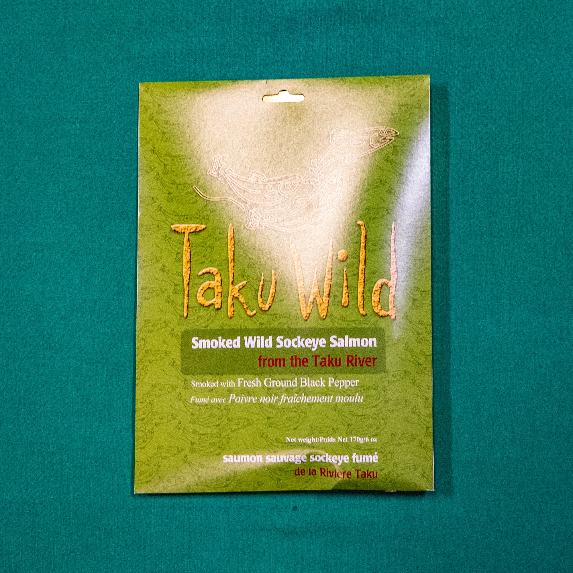 A packet with illustrations of salmon. Text on the image says "Taku Wild. Smoked Wild Sockeye Salmon from the Taku River. Smoked with Fresh Ground Black Pepper." End of image description.