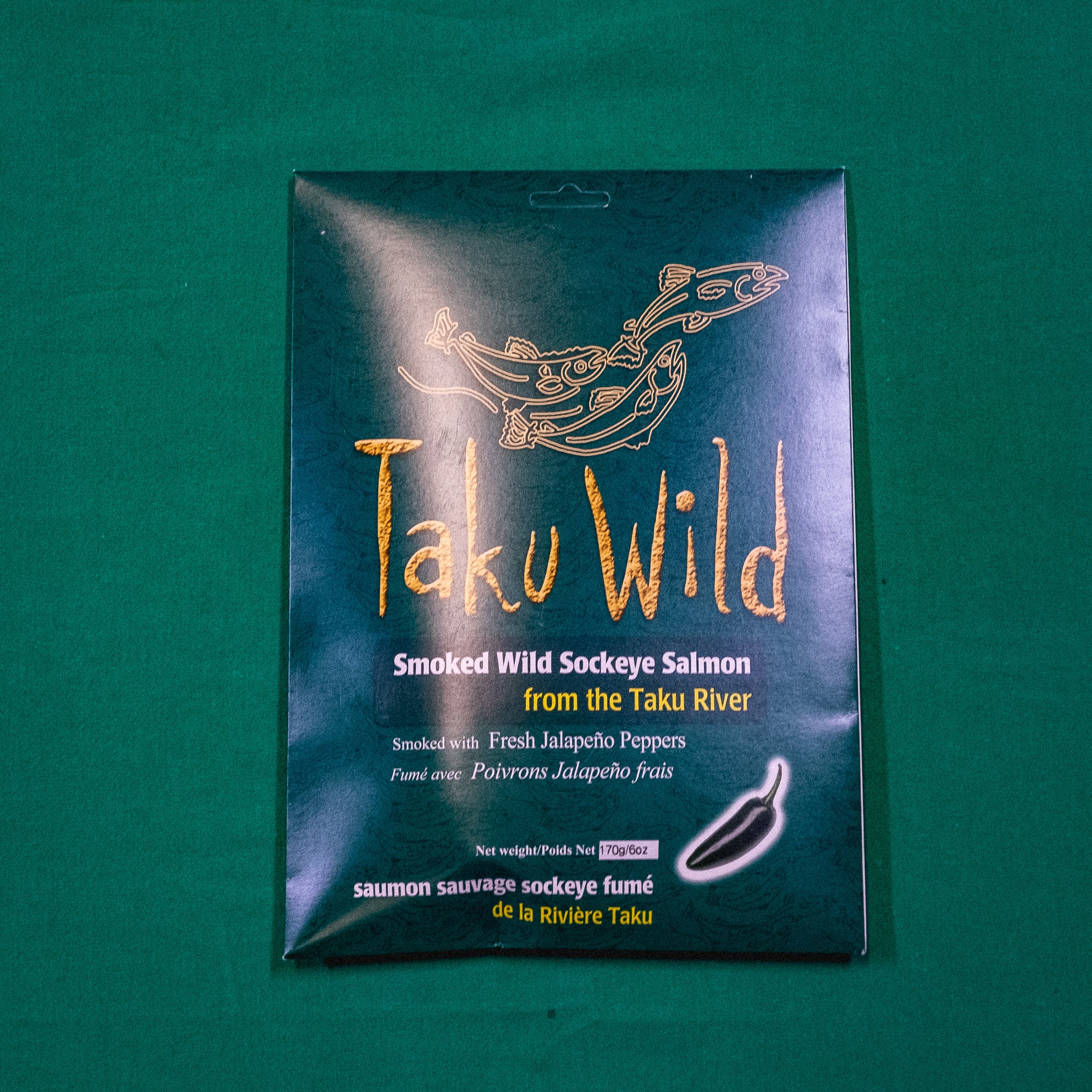 A packet with illustrations of salmon. Text on the image says "Taku Wild. Smoked Wild Sockeye Salmon from the Taku River. Smoked with Fresh Jalapeno Pepper." End of image description.